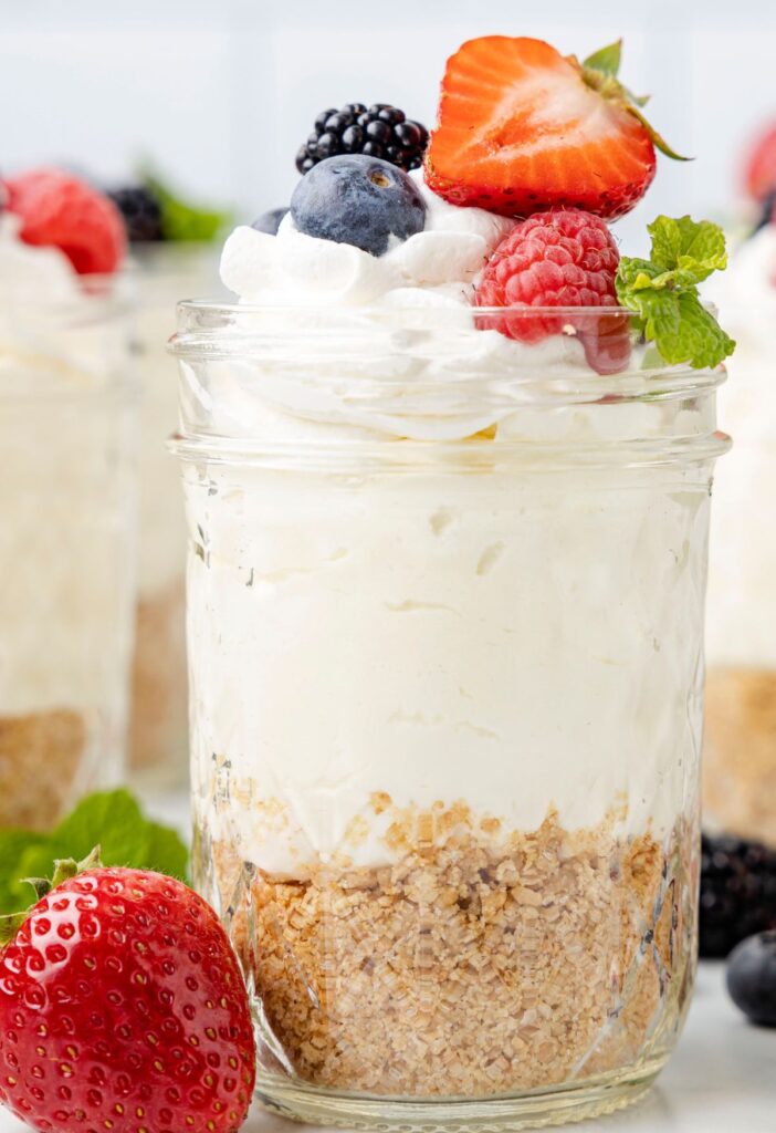 A mason glass jar of cheesecake topped with fresh berries.