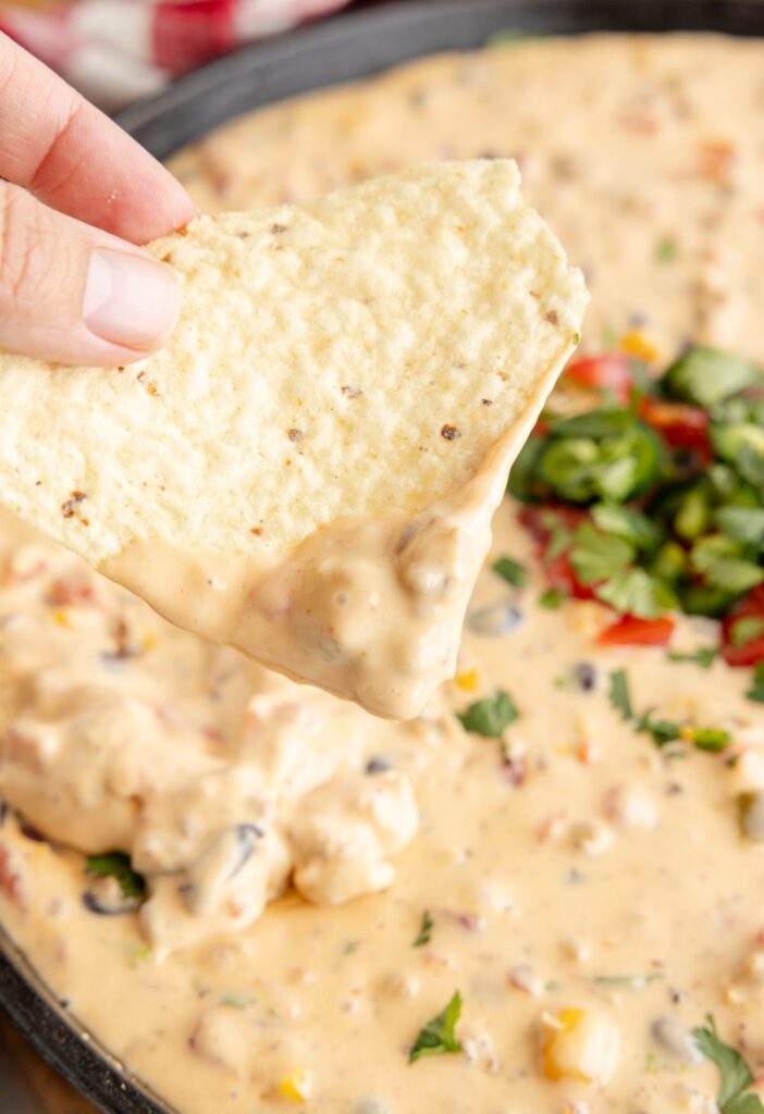 A chip being dipped in the queso, a hand holding the chip. 