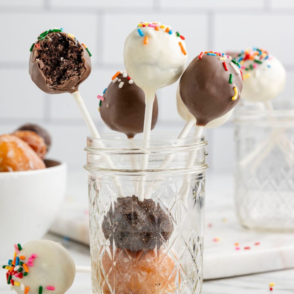 Cake pops in a mason jar with donut holes in the background. 