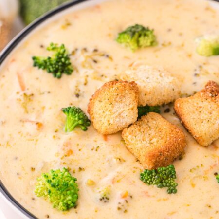 A white serving bowl of soup with croutons on top.