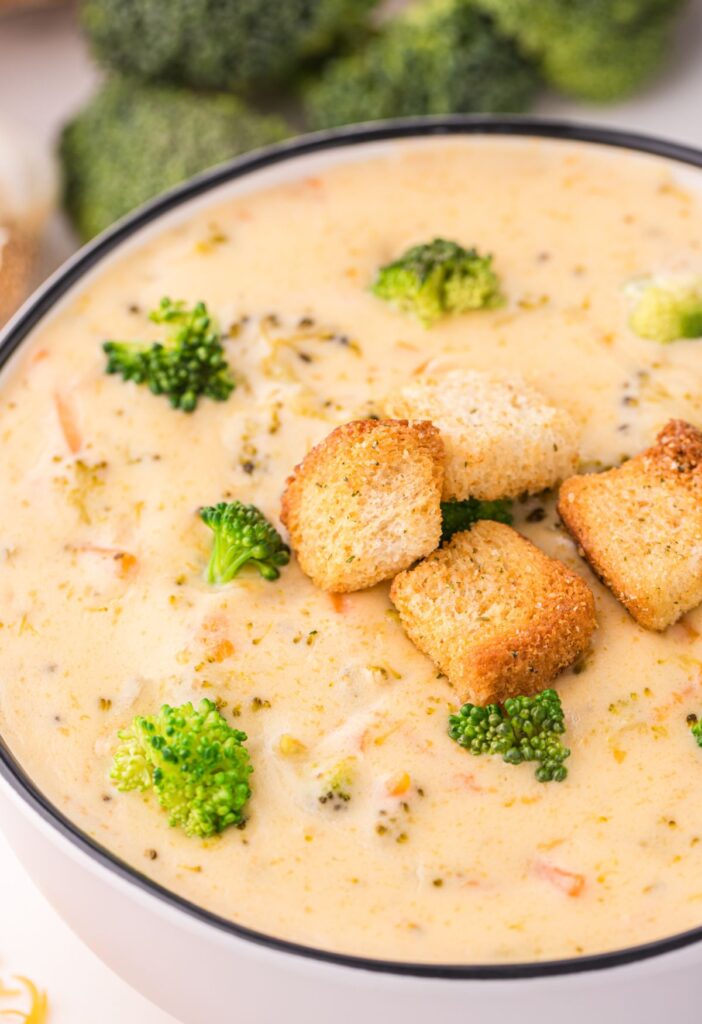 A white serving bowl of soup with croutons on top. 