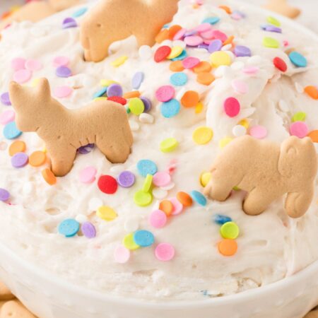 A white bowl of sweet dessert dip with animal crackers on top.