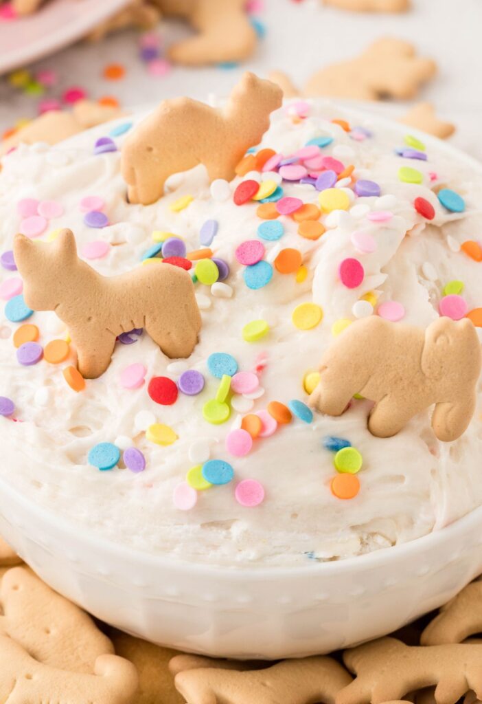 A white bowl of sweet dessert dip with animal crackers on top. 