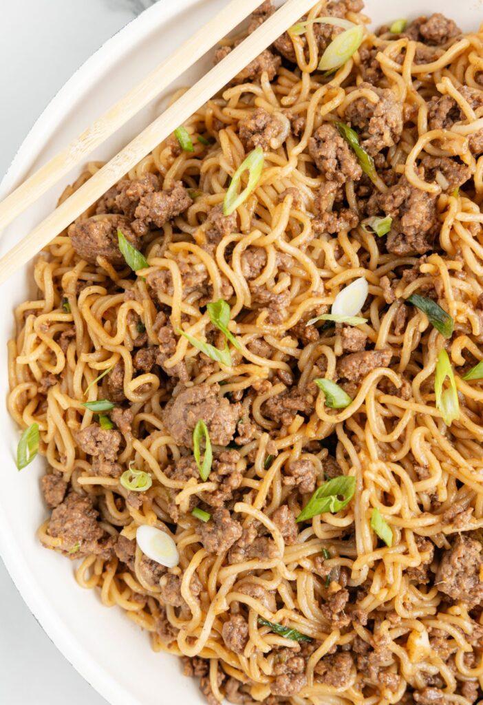 Chopsticks on top of the skillet pan of noodles inside it with beef.