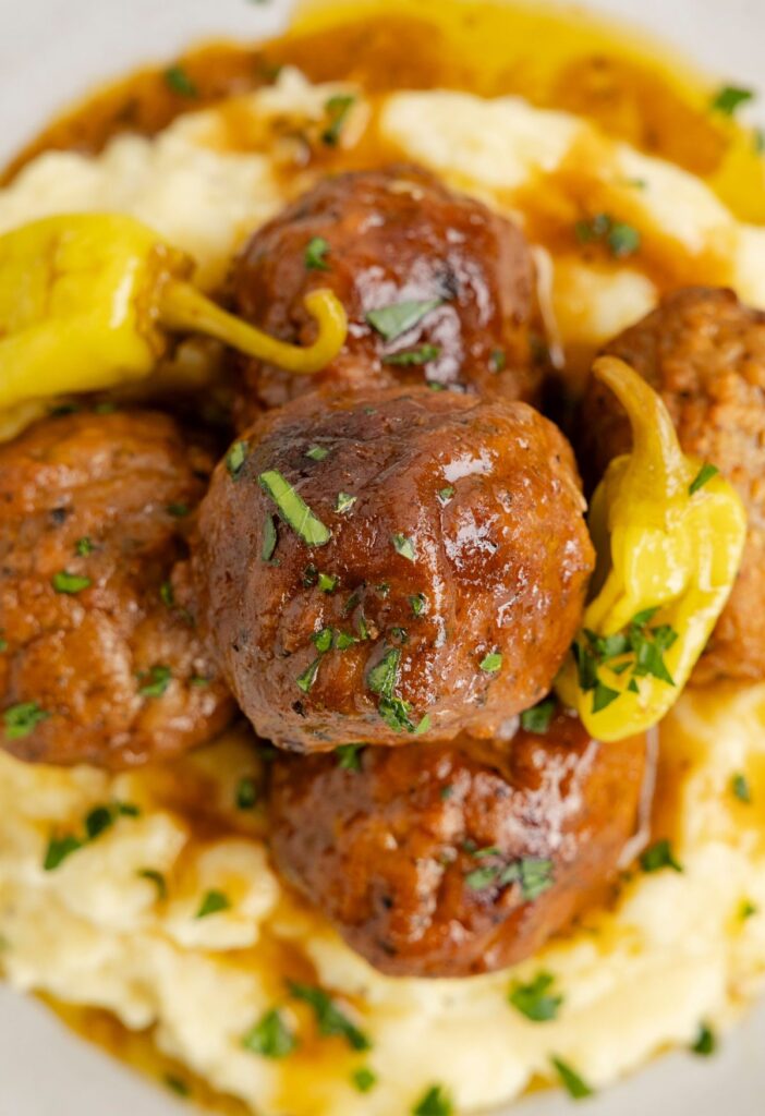 Cooked meatballs on top of potatoes on a white serving plate.