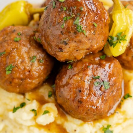 A plate of mashed potatoes and meatballs with sauce and gravy.