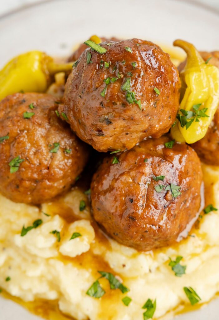 A plate of mashed potatoes and meatballs with sauce and gravy. 