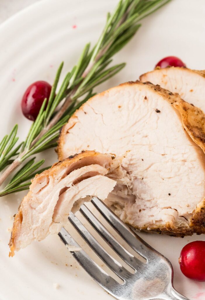 A fork holding some turkey on it over a white plate.