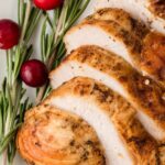 A sliced turkey breast with rosemary and cranberries around it.