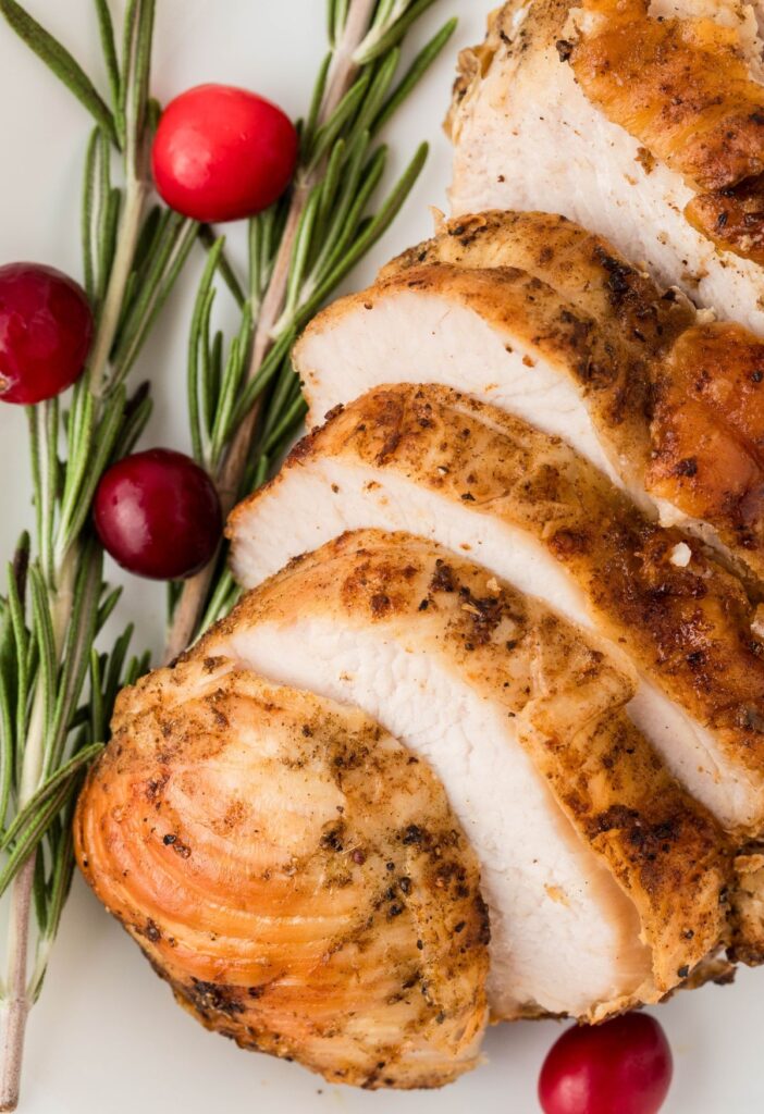 A sliced turkey breast with rosemary and cranberries around it. 