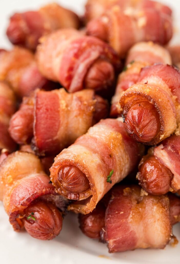 A pile of little sausages wrapped in bacon pieces. 