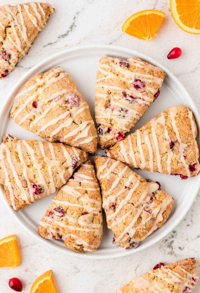 Scones on a white plate with cranberries and oranges around it. 