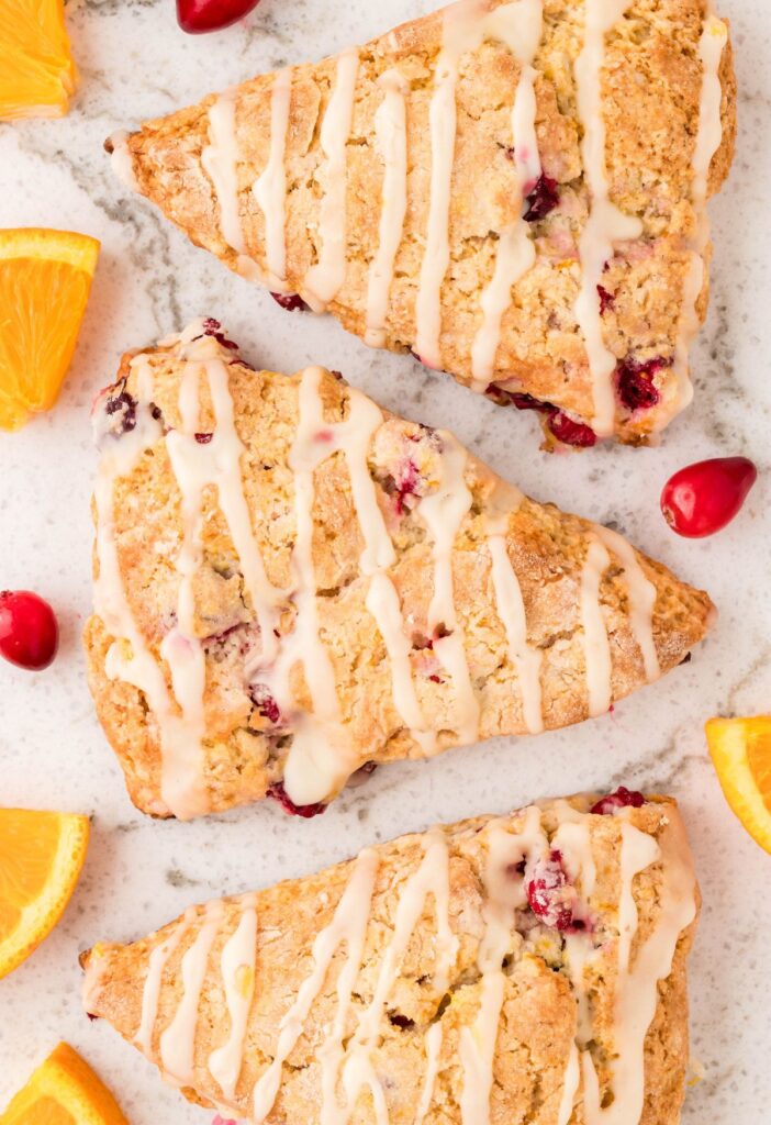 Three scones in a row with cranberry and oranges slices. 