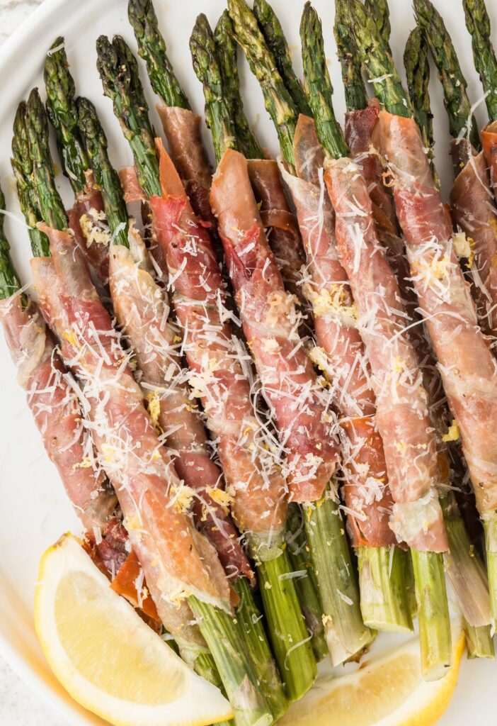 Wrapped asparagus with meat and lemon wedges.