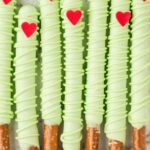 A line up of dipped pretzel rods with a heart and green chocolate.