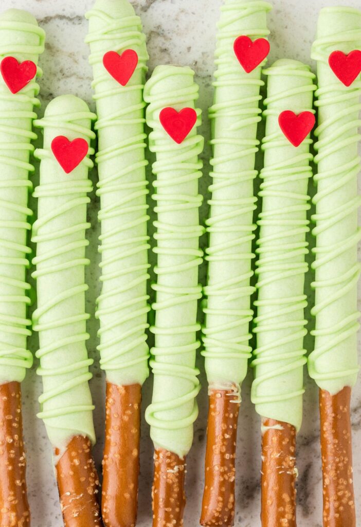 A line up of dipped pretzel rods with a heart and green chocolate. 