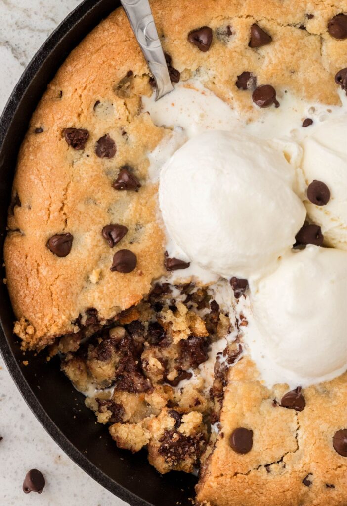 A skillet cookie with a piece taken out of it and a spoon in it. 