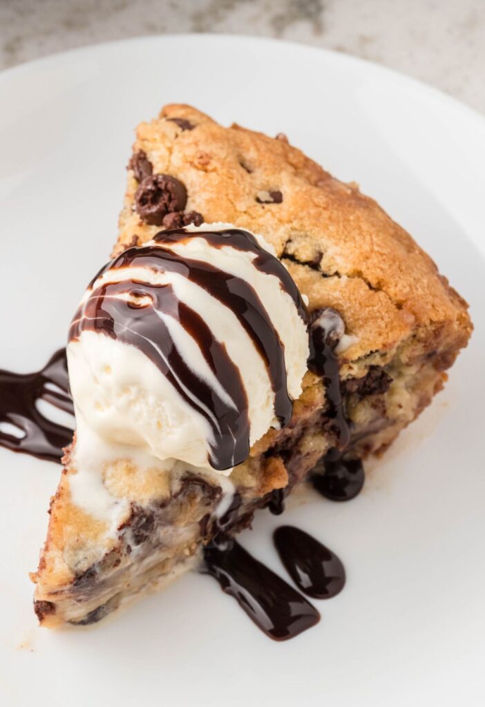 A piece of cookie topped with ice cream and chocolate sauce. 