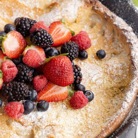 Skillet pan with a pancake, fresh berries, and powdered sugar in it.