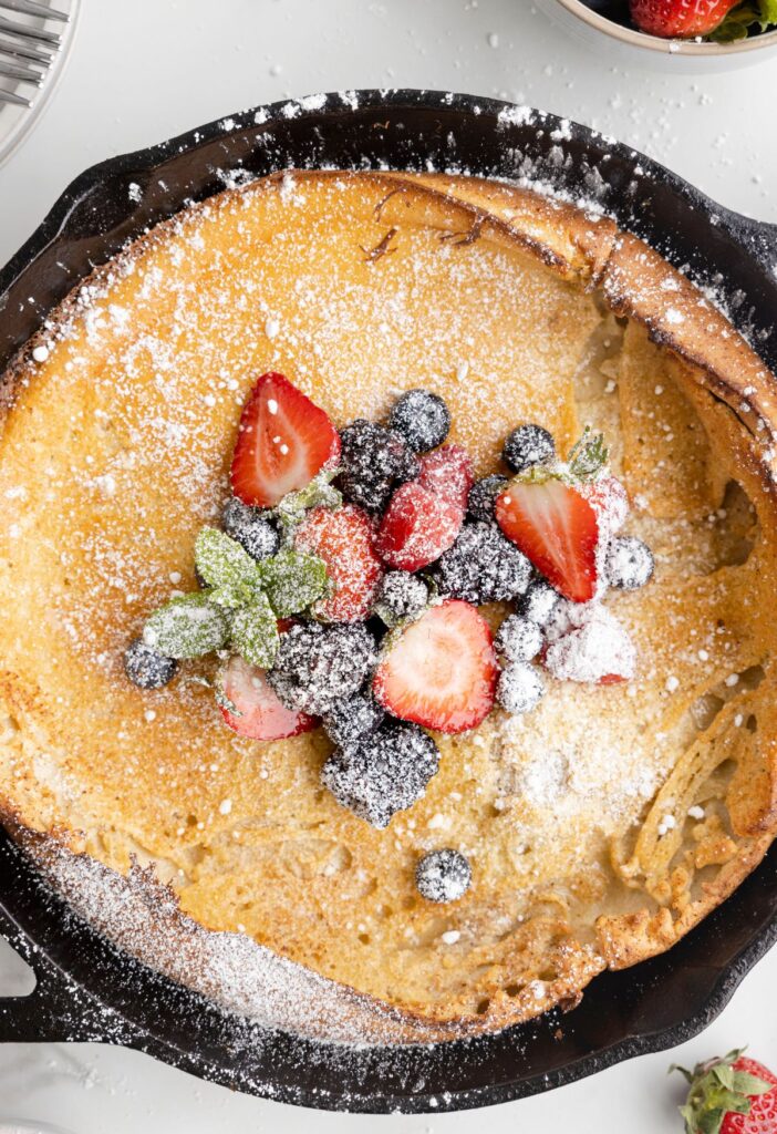 A cooked dutch baby with berries, powdered sugar, in a cast iron skillet. 