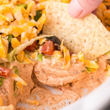 Layered taco dip inside a serving dish with a chip
