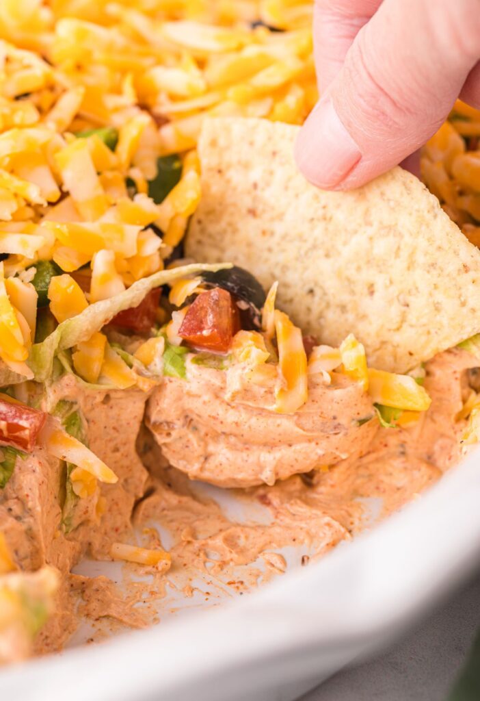 Layered taco dip inside a serving dish with a chip