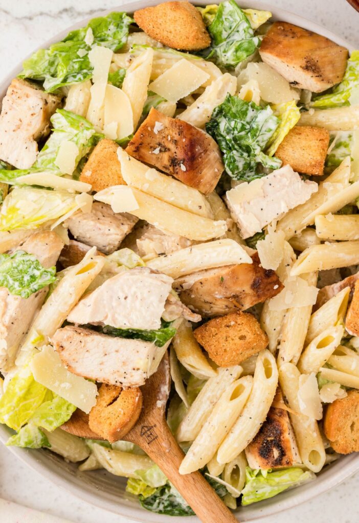 A chicken pasta salad with a serving spoon in it. 