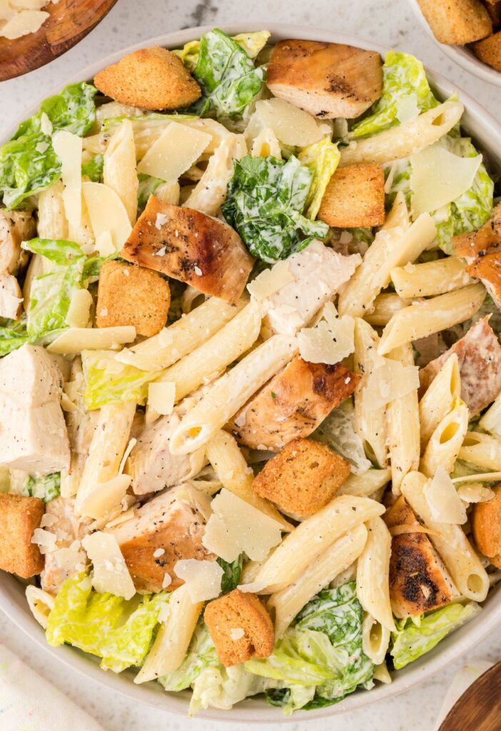 Close up off the top of the bowl of pasta salad with lettuce, chicken, and caesar dressing. 