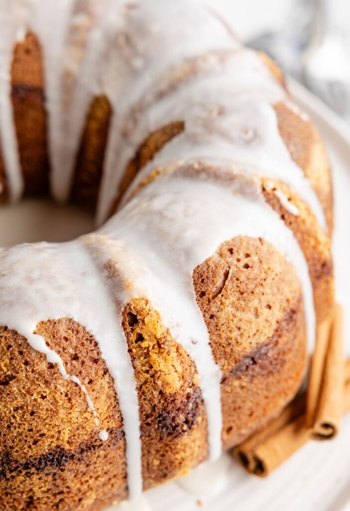 A cooked bundt cake with a glaze and cinnamon sticks to the side of it.