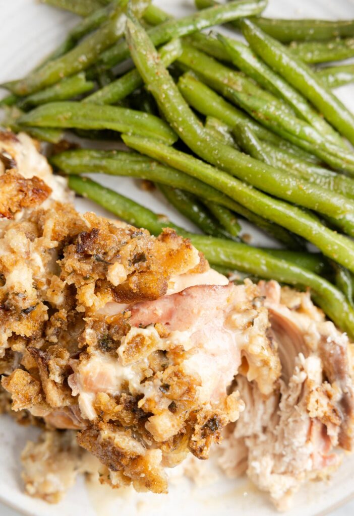 A serving plate of chicken and ham with green beans next to it. 