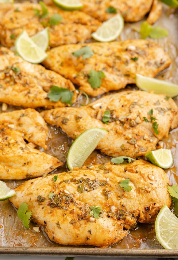 Cooked chicken breasts on a sheet pan with lime wedges. 