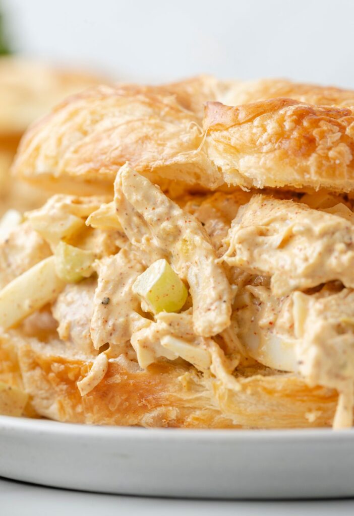 Southern style chunky chicken salad inside a croissant on a white plate.
