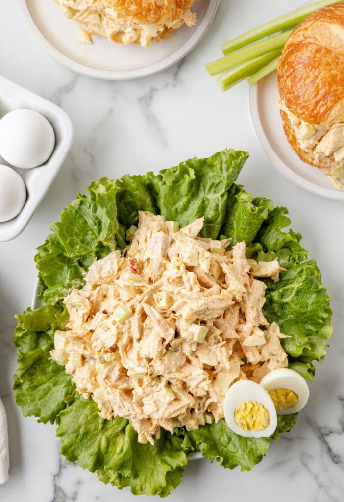 Creamy chunky chicken salad on green lettuce with eggs in the background.