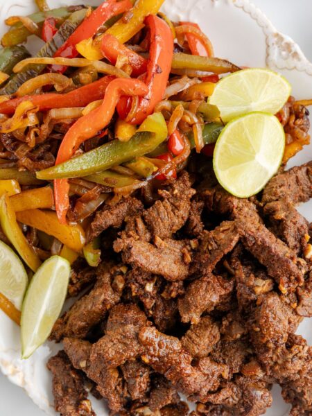 A white platter of steak meat for fajitas and vegetables.