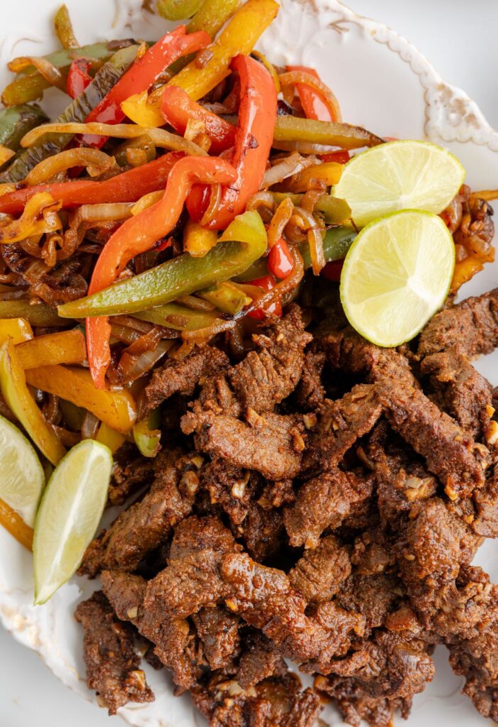 A white platter of steak meat for fajitas and vegetables. 