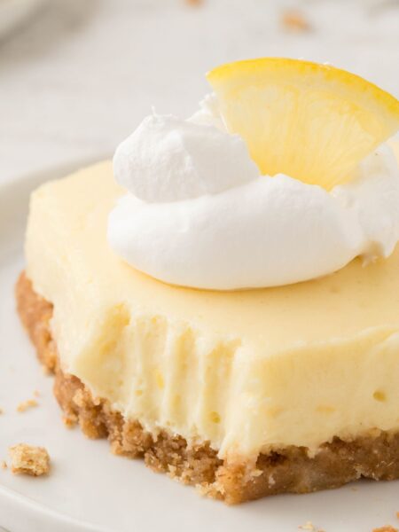 One square of cheesecake bar with whipped cream and a lemon wedge.