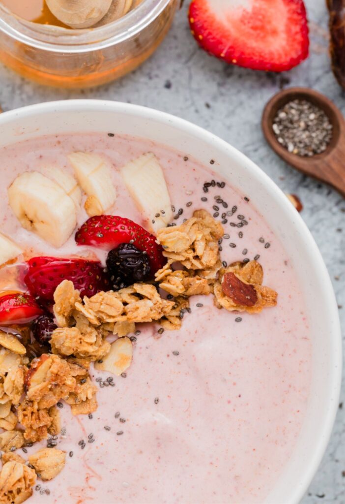 A close up of the smoothie bowl with toppings on it and to the side of the bowl. 