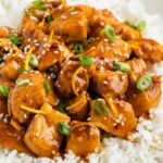 Sweet glazed orange chicken on top of a bed of white rice.