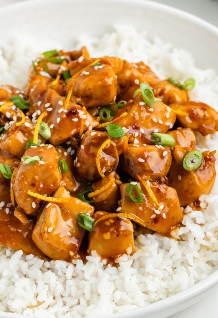 Sweet glazed orange chicken on top of a bed of white rice. 