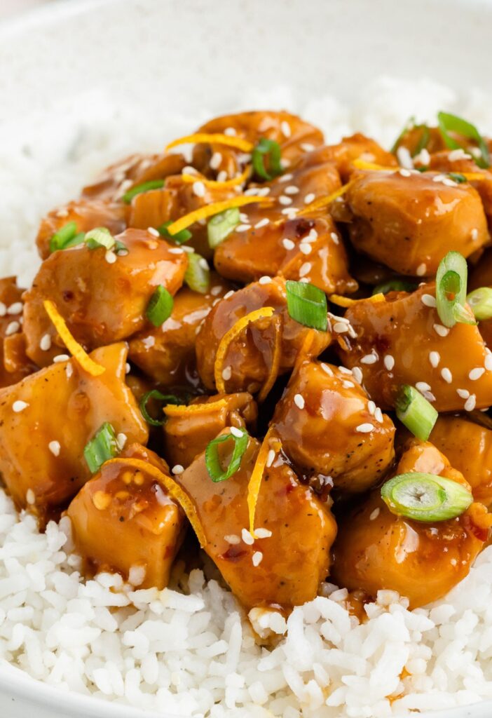 Finished orange chicken dish served over rice and garnished with green onions. 