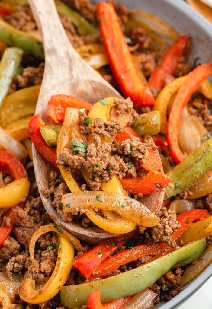 A skillet pan of the fajita filling with a wooden spoon