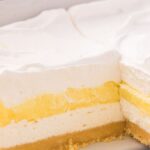 A pan of the lemon lush dessert with a piece gone to show the layers