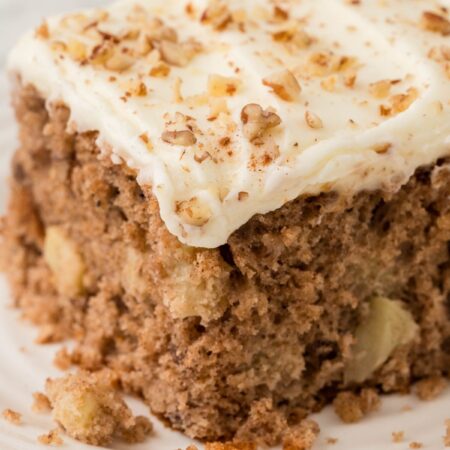 A slice of apple cake with frosting on a white plate.