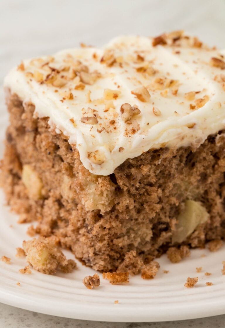 A slice of apple cake with frosting on a white plate.