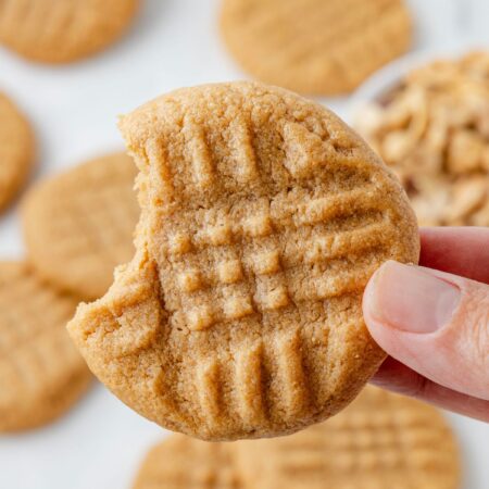 A hand holding one peanut butter cookie with a bite taken out of it