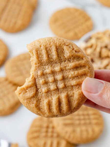 A hand holding one peanut butter cookie with a bite taken out of it