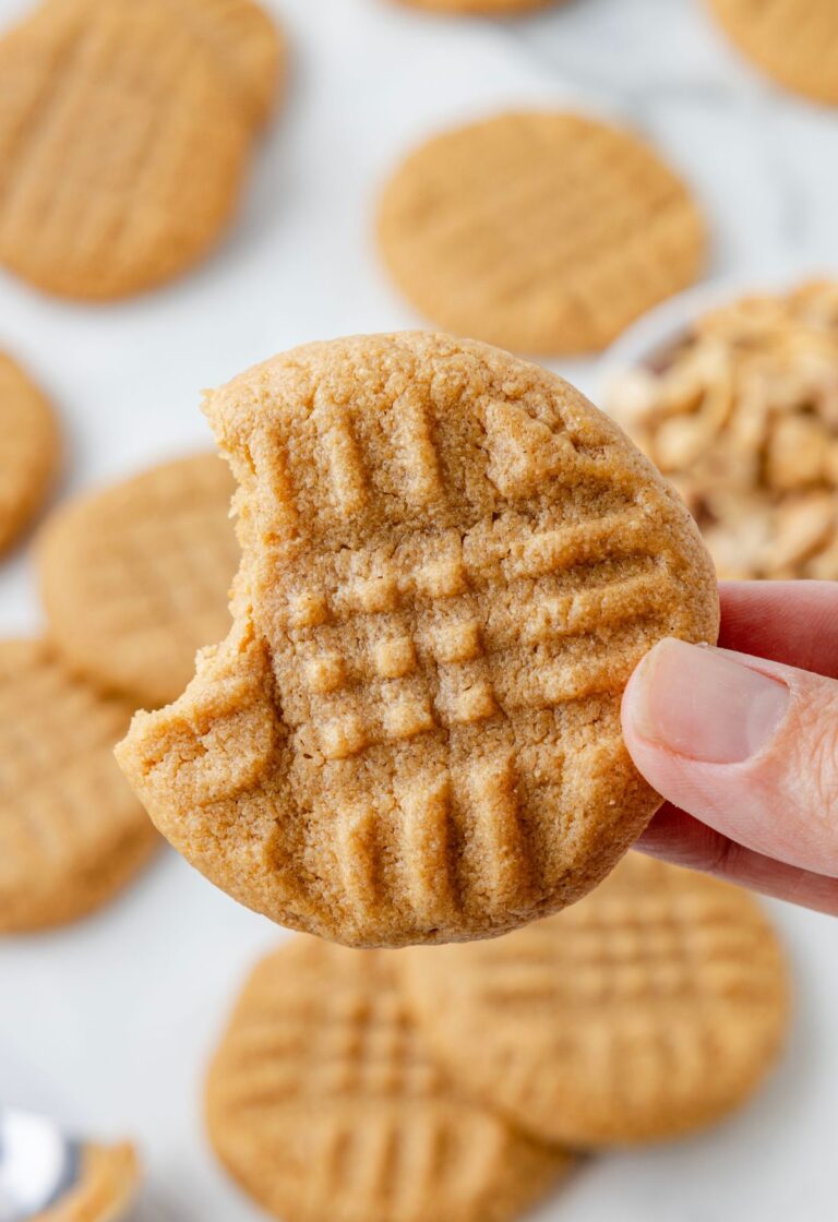 A hand holding one peanut butter cookie with a bite taken out of it