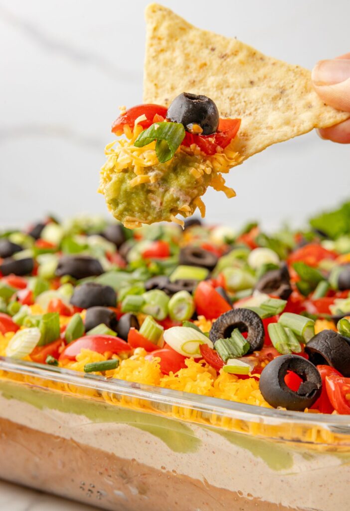 A chip with some dip on it above the pan of 7 layer dip