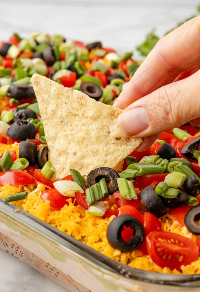 A chip dipping inside the pan of layered taco dip