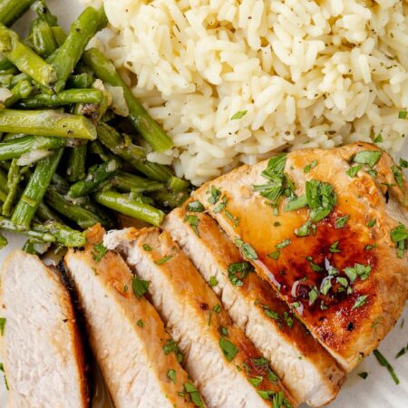 Sliced pork chop on a plate with rice and asparagus as sides.